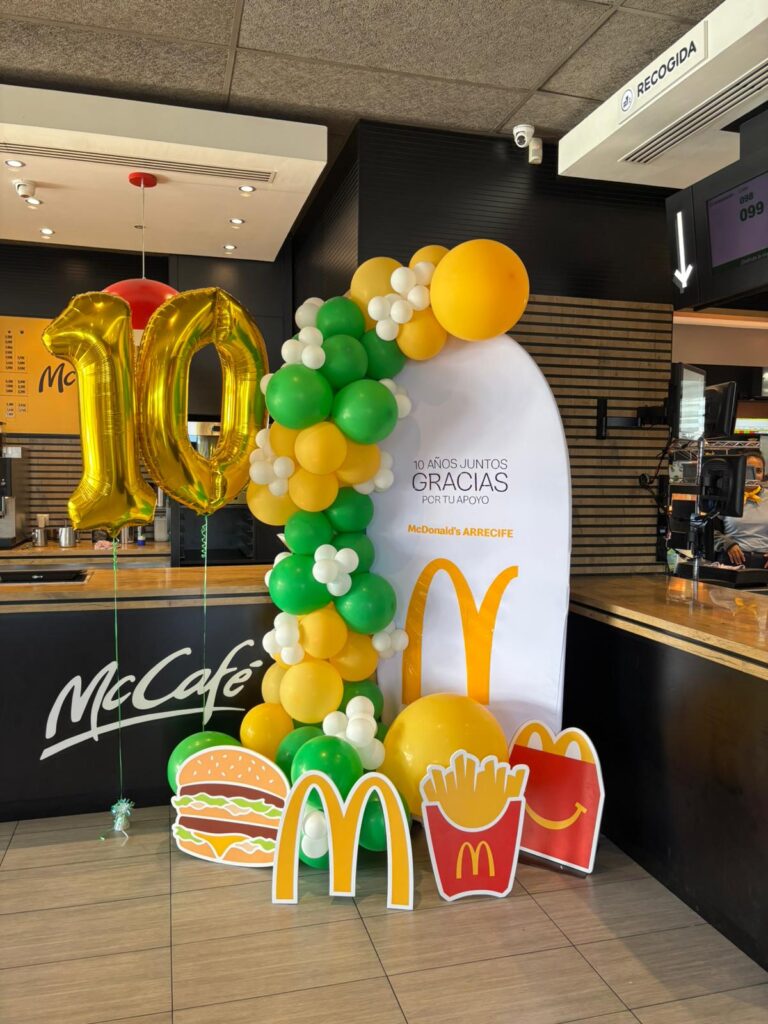 Colorido decorado de celebración con globos en tonos amarillo, verde y blanco, incluyendo un letrero de agradecimiento y figuras de McDonald's para celebrar un 10º aniversario en un establecimiento de comida rápida.