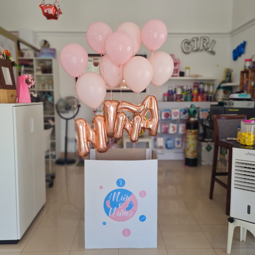 Globos con letras para celebración de maternidad en tonos rosados y dorados en tienda de artículos para fiestas y regalos.
