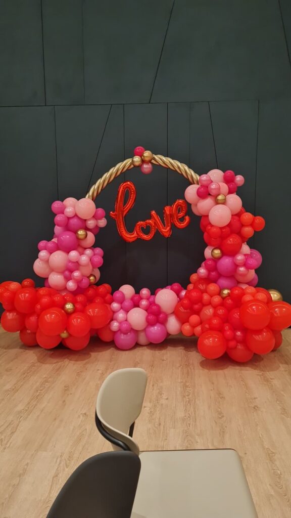 Ramillete de globos en tonos rosas y rojos con la palabra "love" en globo de letras rojas, decorando un evento romántico o celebración especial.